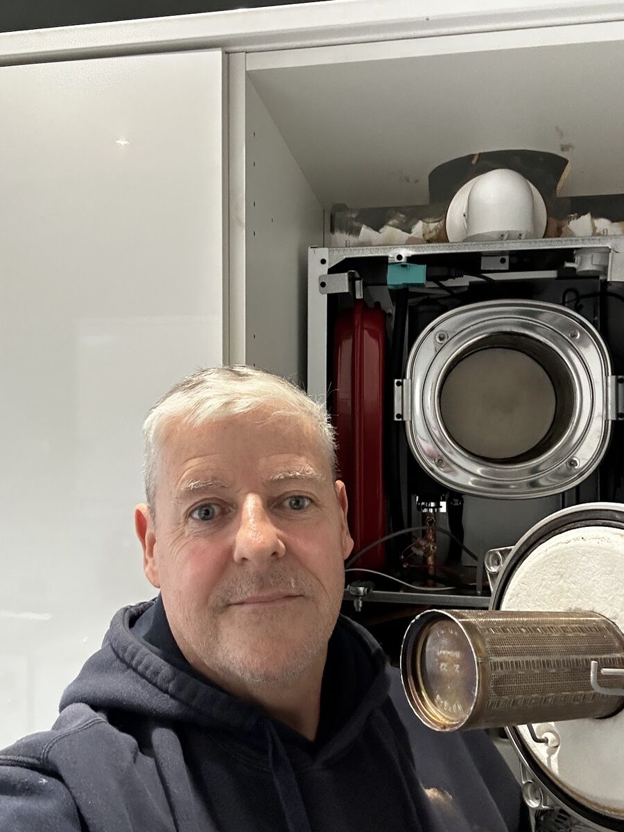 Person beside an open wall-mounted boiler, illustrating a service inspection.